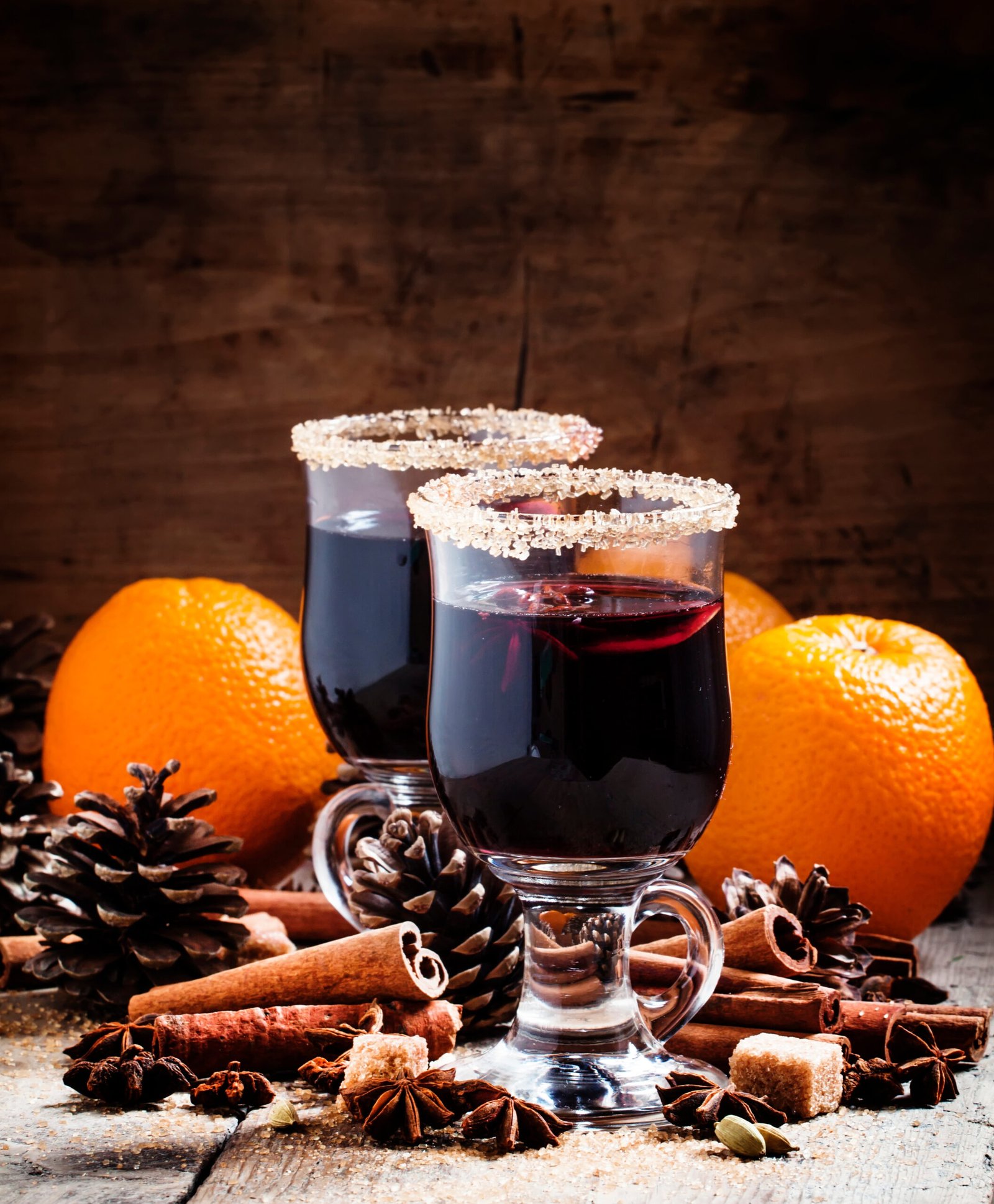 Mulled wine in large glasses, spices, oranges and fir cones on a dark wooden background, selective focus